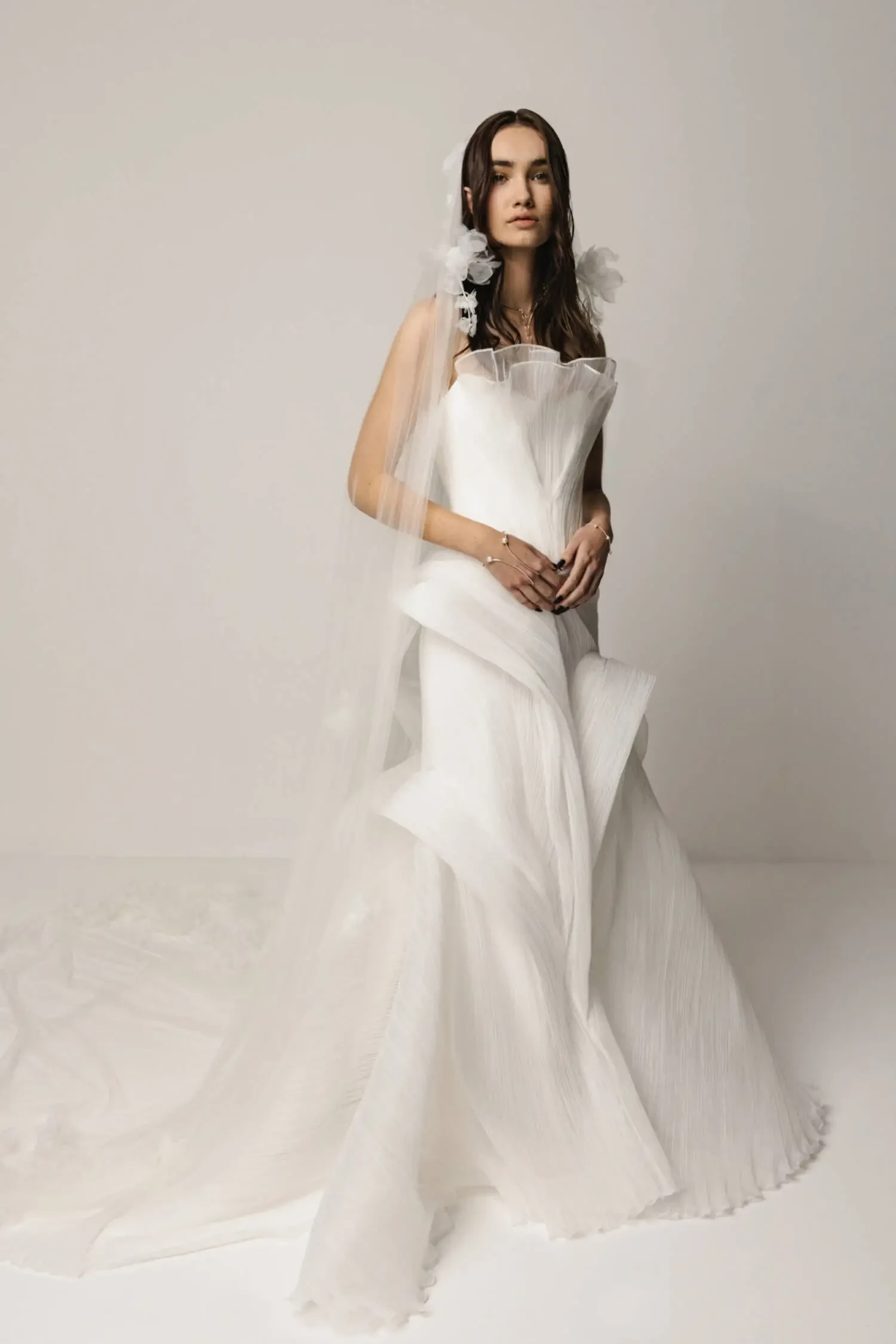 Model is wearing a pleated organza gown with a sculpted corset bodice and full cascading train