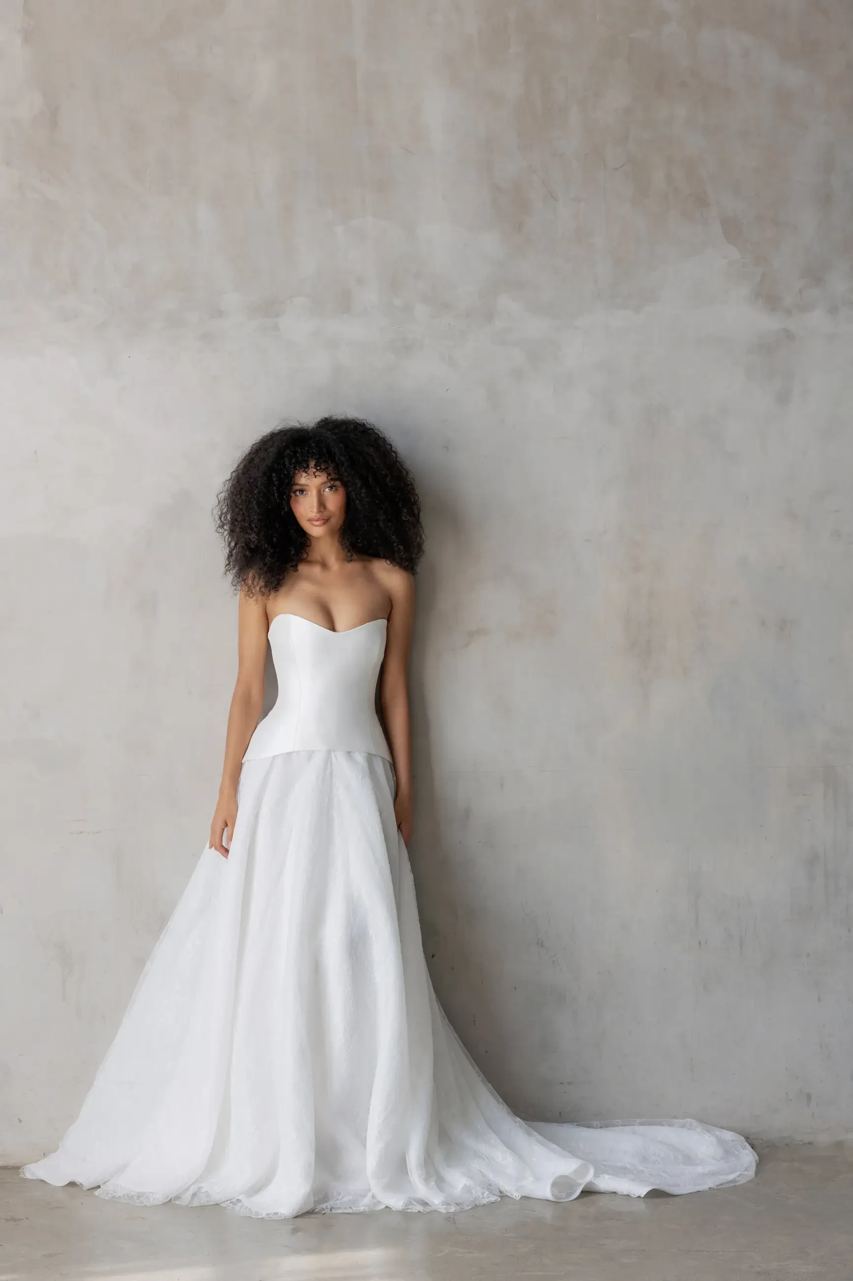 Model is wearing a two-piece gown with a sculpted Mikado bodice and a flowing lace and organza skirt that creates soft movement.