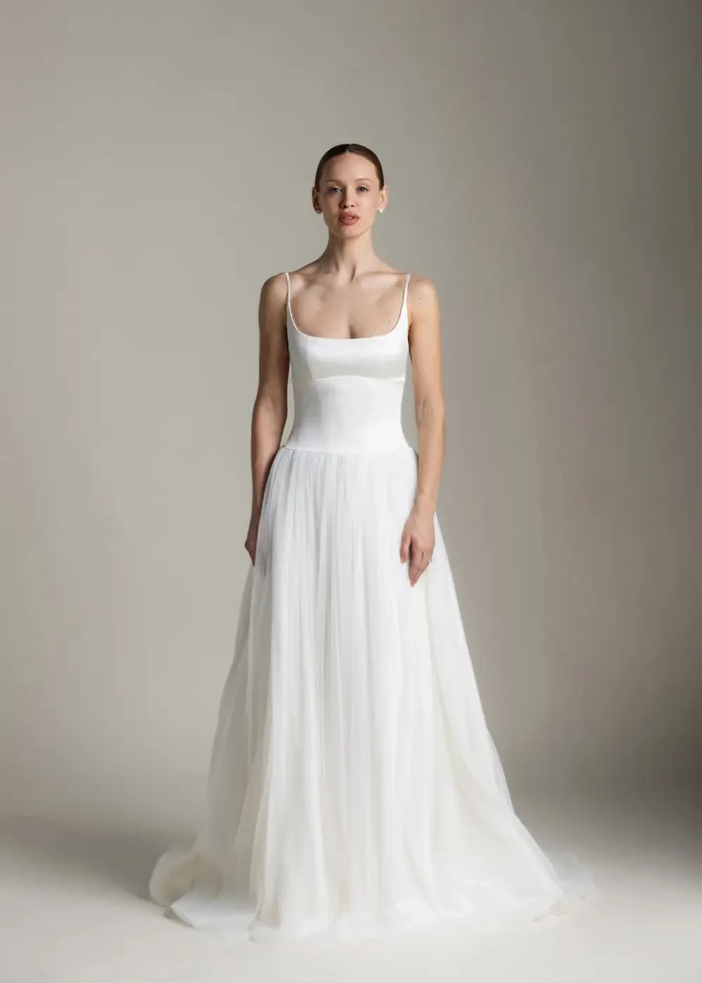 A woman in a white gown stands against a neutral background.