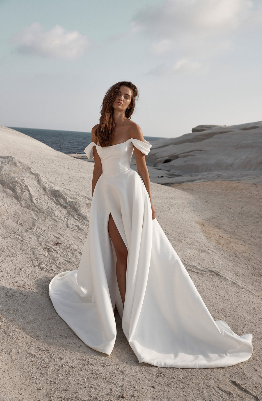 Model is wearing a luminous duchess satin ballgown with a structured bodice, plunging low back, and a full skirt that can feature a split.