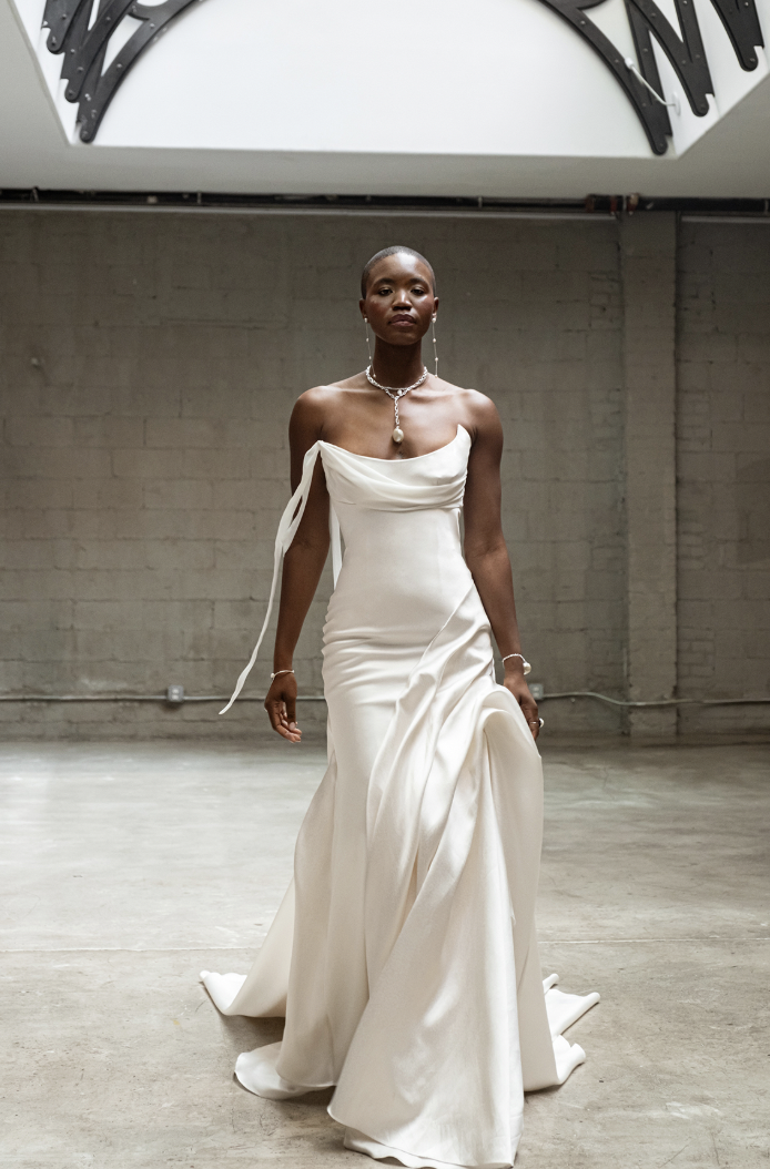 A model wearing a sleek, white gown walks confidently in a spacious, industrial-style setting.