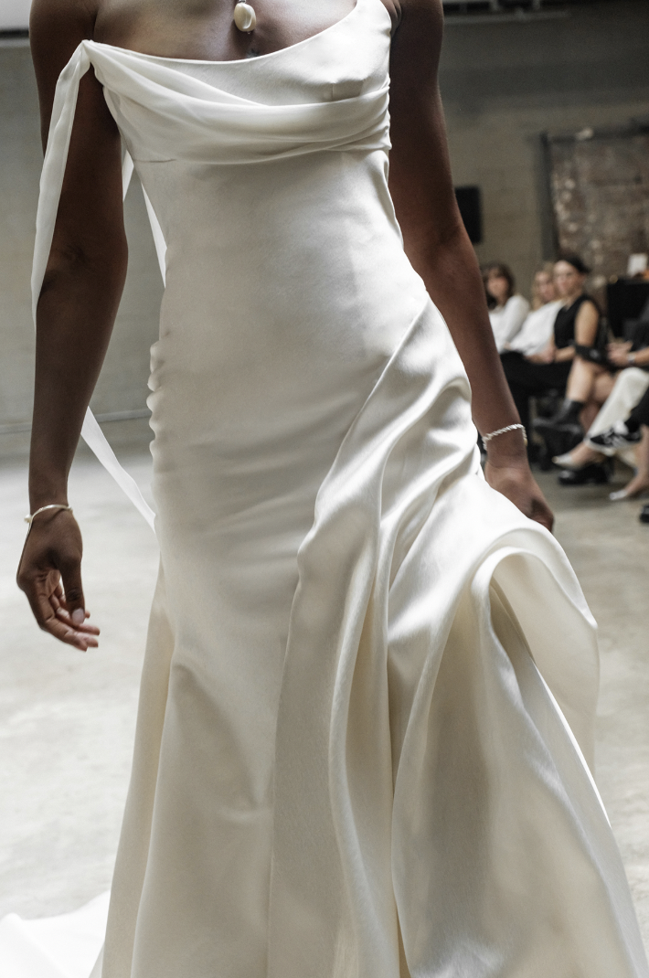A model wearing a sleek, white gown walks confidently in a spacious, industrial-style setting.